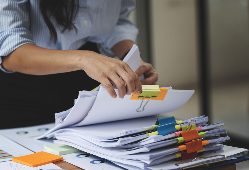 Person organising stacks of printed reports and schedules with paper clips, symbolising outdated manual processes that Timegrip replaces with digital workforce planning and time tracking.