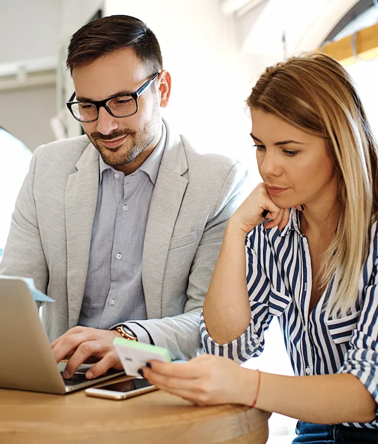 Two hotel department managers collaborate at a café, reviewing financial details on a laptop while discussing a payment card transaction.