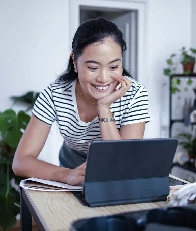 A smiling professional in a striped shirt leans on a wooden desk while working on a tablet with a keyboard, engaged in a productive workplace discussion in a modern office.