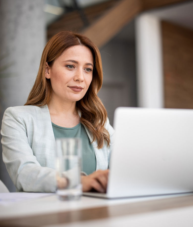 Professional woman managing employee schedules on a laptop in a modern office setting.