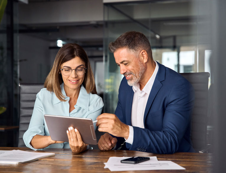 Two colleagues collaborating on a tablet in a modern meeting room, representing teamwork and efficient workforce management and scheduling
