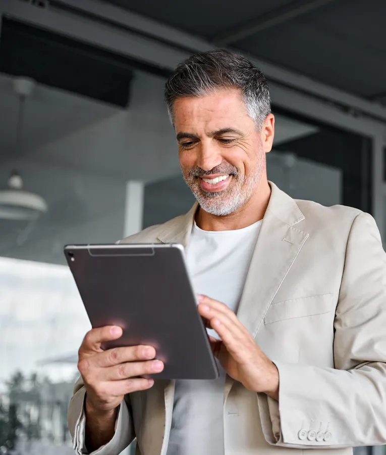 Smiling middle-aged professional in beige blazer using a tablet outdoors, representing mobile workforce solutions, digital management tools, and flexible work environments.