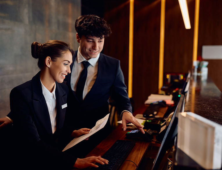 A hotel manager and staff member reviewing guest service operations at the front desk.