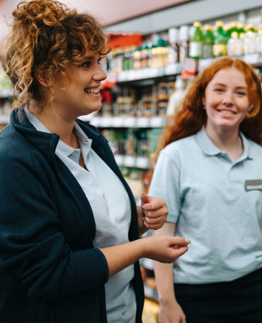 Two smiling supermarket employees working in-store, scheduled via digital workforce planning tools to ensure optimal retail coverage and efficient time tracking.