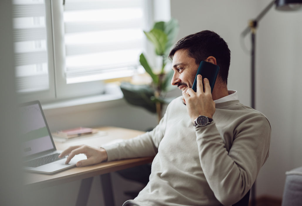 An employee works from home, talking on the phone while using a laptop – illustrating flexible working hours, digital time tracking, and strong communication in modern work environments.