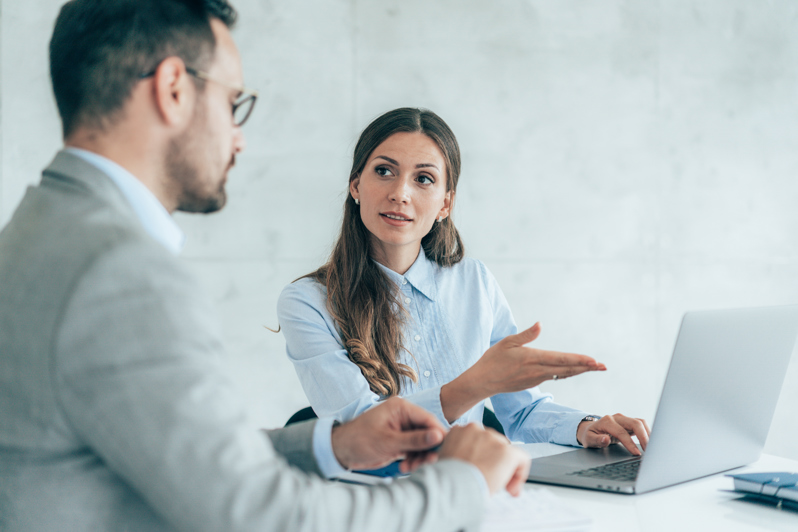 Two colleagues discussing AI-based workforce management in front of a laptop, focusing on smarter staff scheduling and time tracking in the workplace.