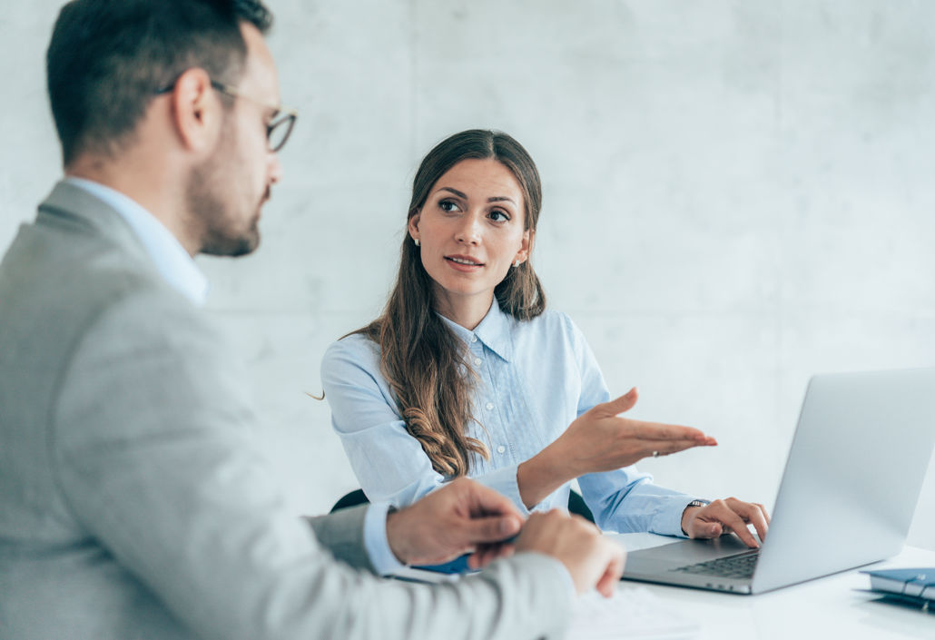 Businesswoman explaining a digital workforce management solution to a colleague during a meeting, highlighting tools for time tracking and shift scheduling.