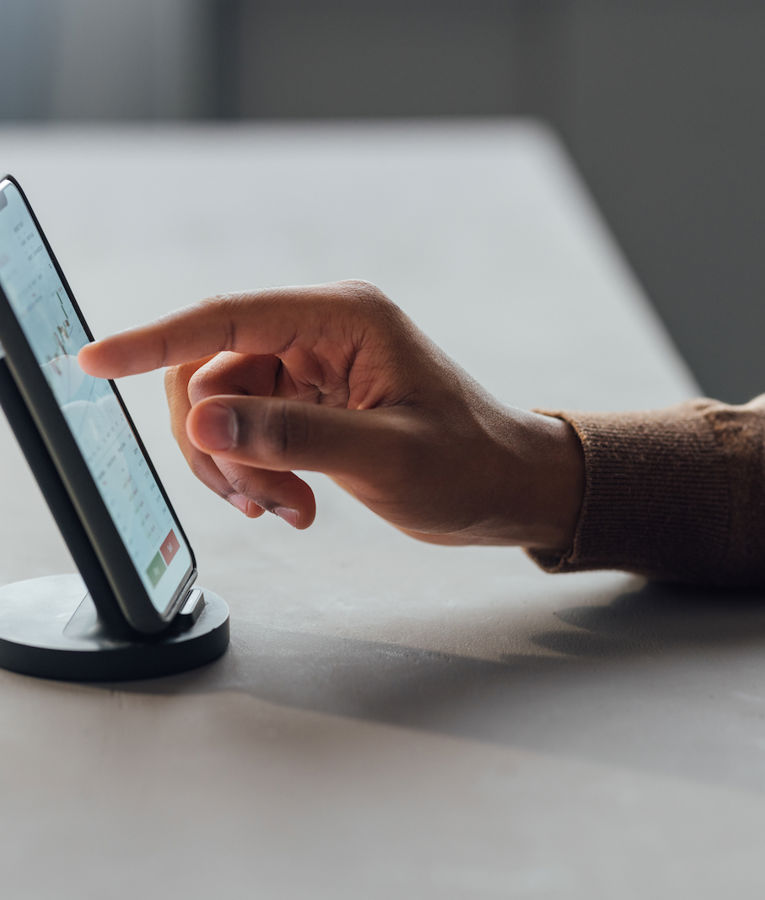 Close-up of a person using a smartphone on a stand, interacting with a financial or data analysis app displaying charts and graphs. Ideal for content related to mobile workforce management, productivity apps, or digital business tools.