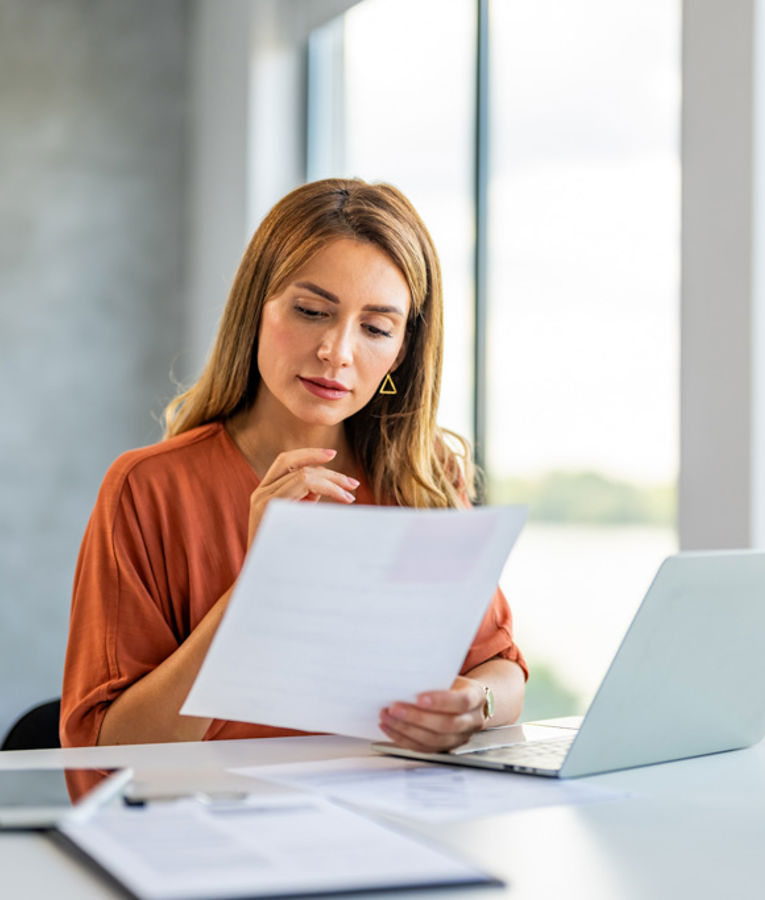 Woman reviewing documents at a laptop in a modern office environment, representing data-driven workforce management and scheduling