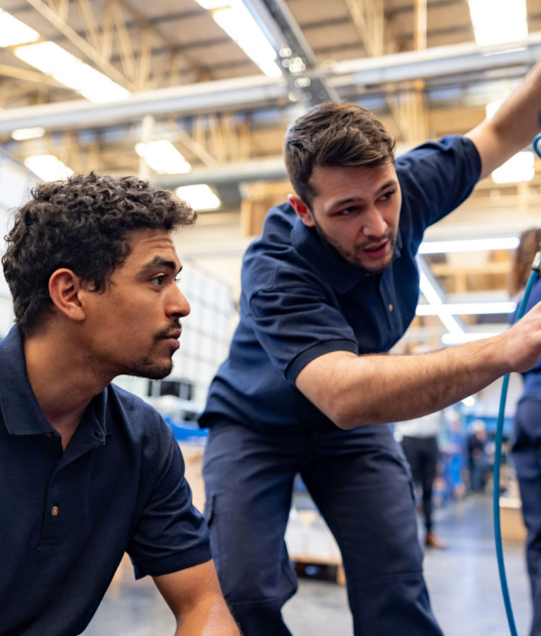 Two industrial technicians in navy uniforms collaborating on equipment maintenance in a factory, highlighting skilled labour, workforce training, and technical operations.