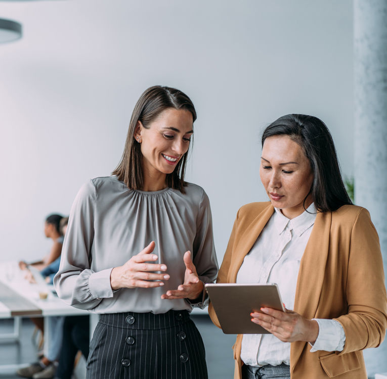 Two professional women collaborating using a tablet in a modern office setting.