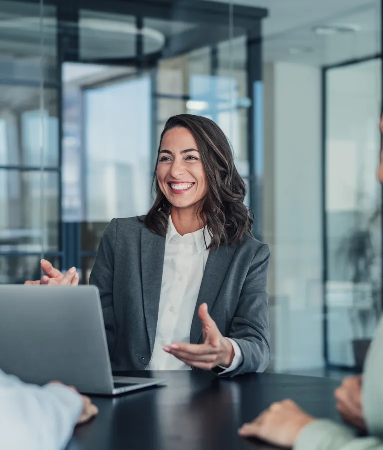 Smiling business professional presenting workforce management strategies to colleagues in a meeting room, with focus on staff scheduling and digital time tracking.