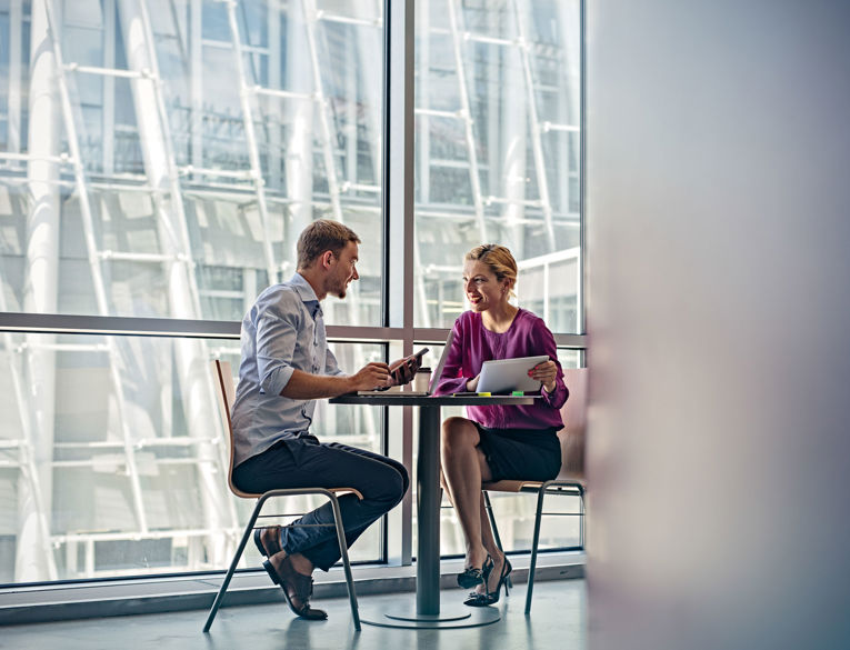 Two colleagues in a modern office building discussing workforce management and scheduling using digital solutions.