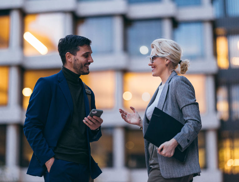 Two colleagues in a business setting discussing workforce management, scheduling, and time tracking using a mobile device