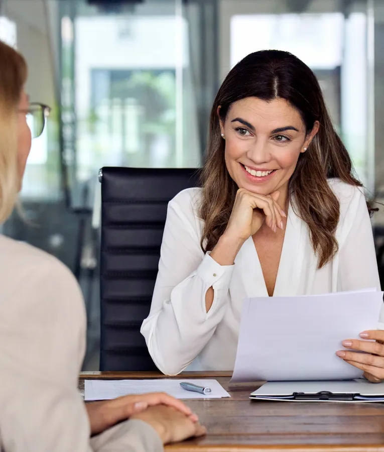 Smiling HR manager conducting a job interview in a modern office, reviewing documents and engaging with a candidate. Represents effective recruitment and talent acquisition.