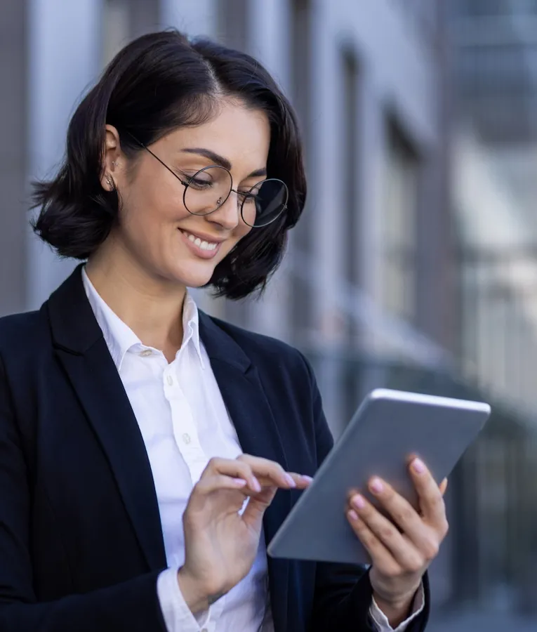 Smiling businesswoman using a tablet outdoors, managing tasks and workforce operations remotely. Represents mobile workforce management and digital productivity.