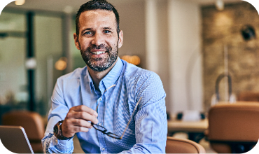 Manager smiling at desk with screen nearby – real-time insights into time tracking, staffing and employee status.