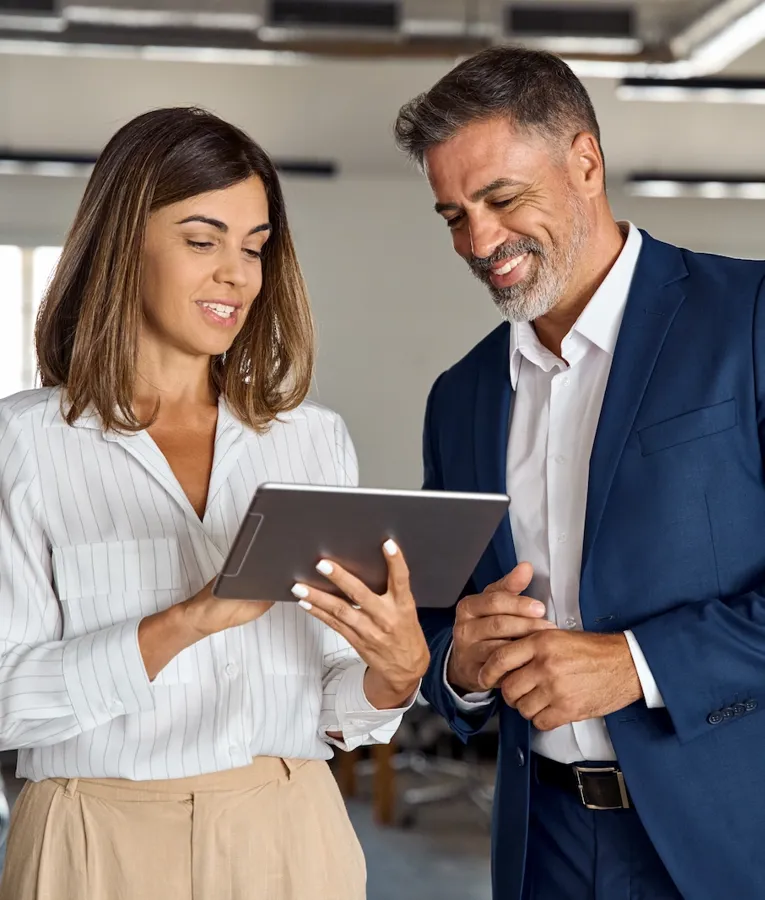 Smiling business professionals reviewing workforce scheduling on a tablet in a modern office, improving efficiency and collaboration.